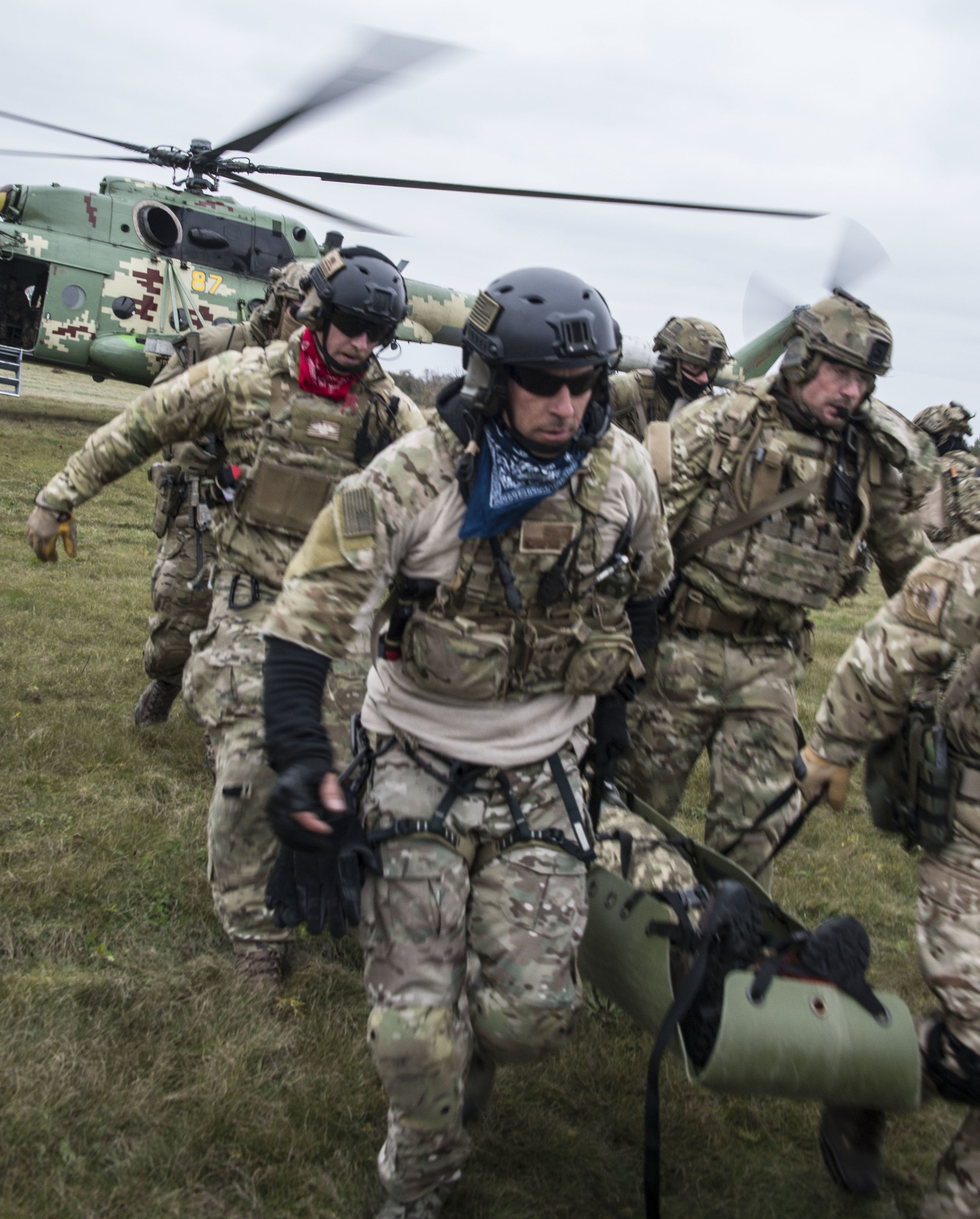Airmen carry a litter with a helicopter in background.