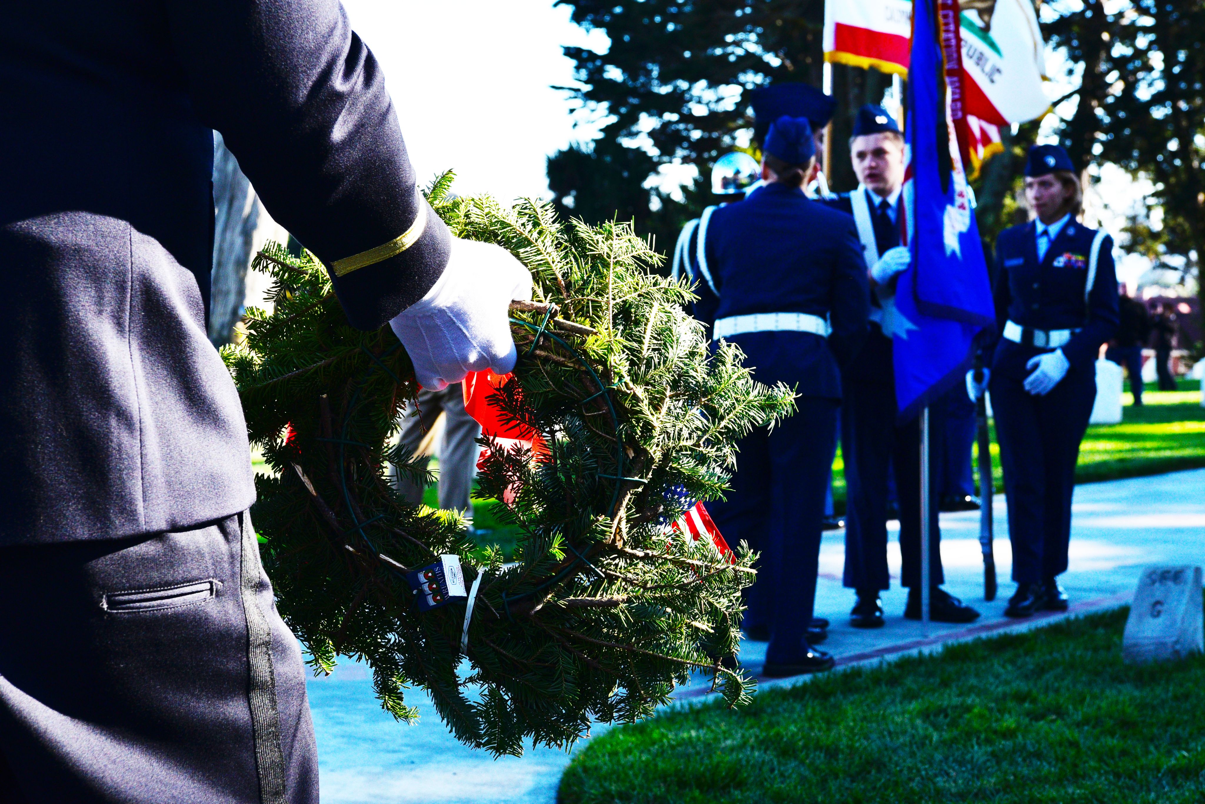 A soldier holds a wreath with white gloves. 