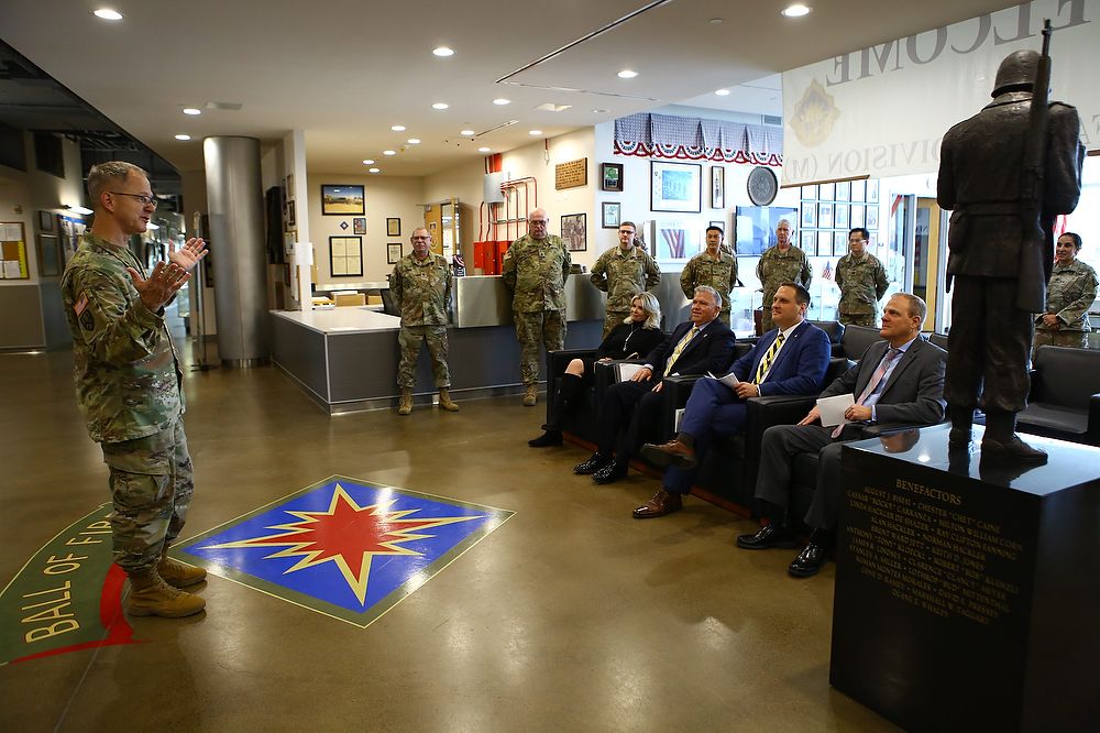 Army officer stands and speaks to group of men in suits.