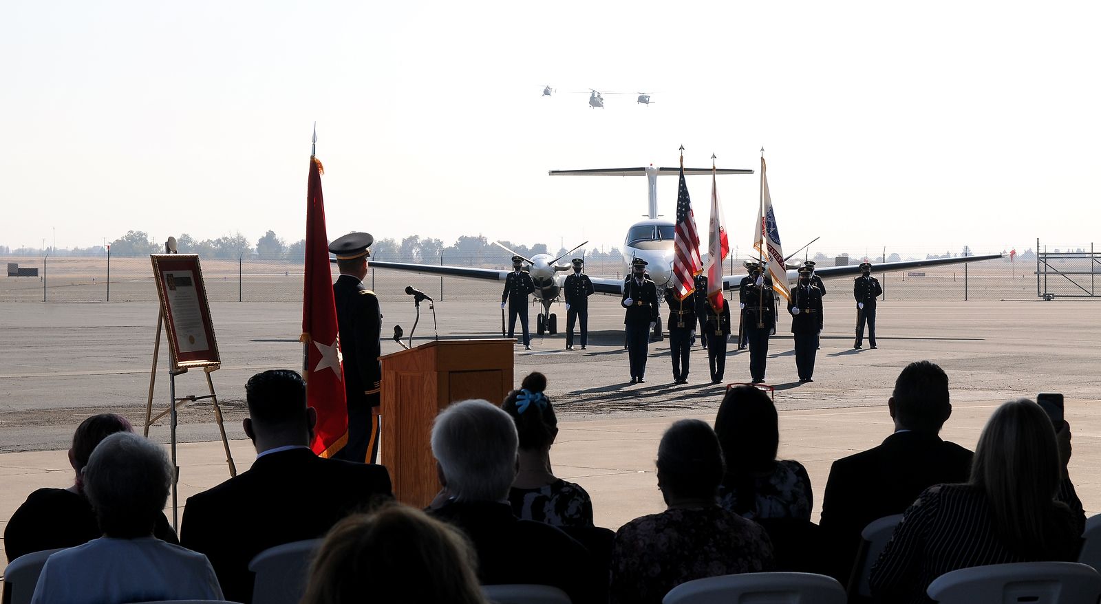 Helicopters fly over honor guard and crowd.