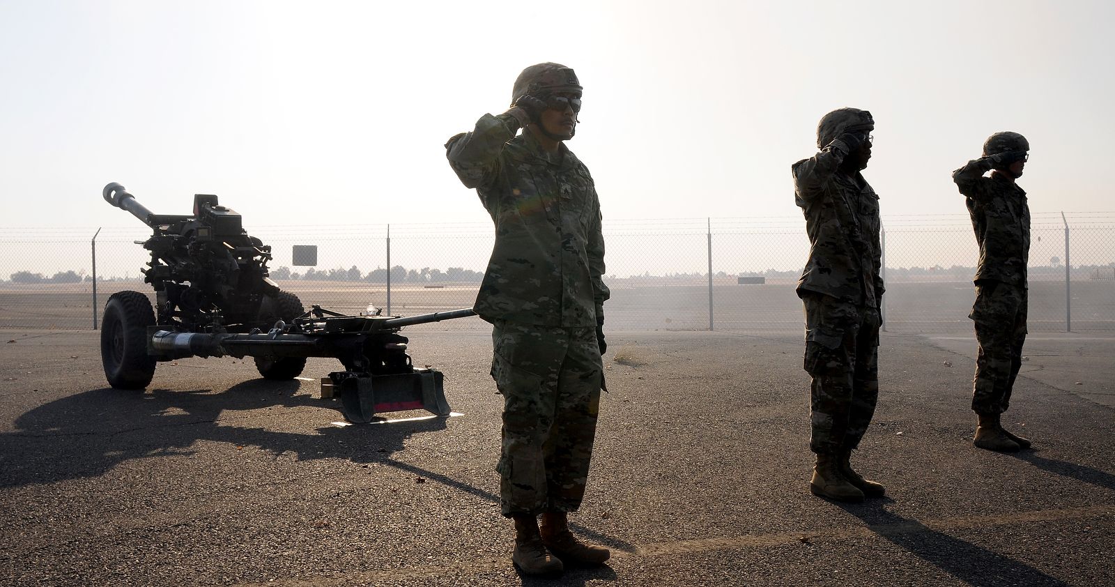 Soldiers salute while standing next to cannon.