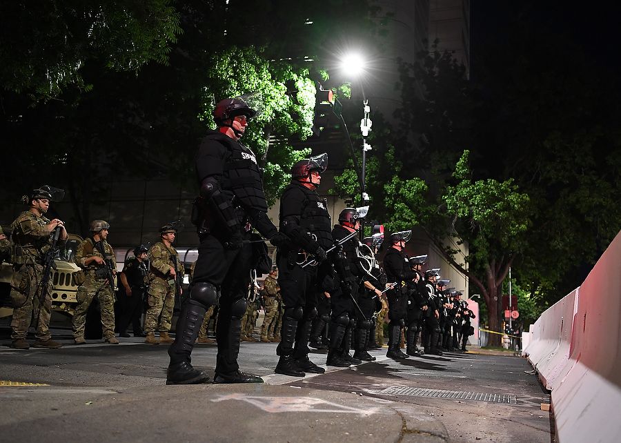 Armed soldiers stand behind line of local law enforcement on a city street