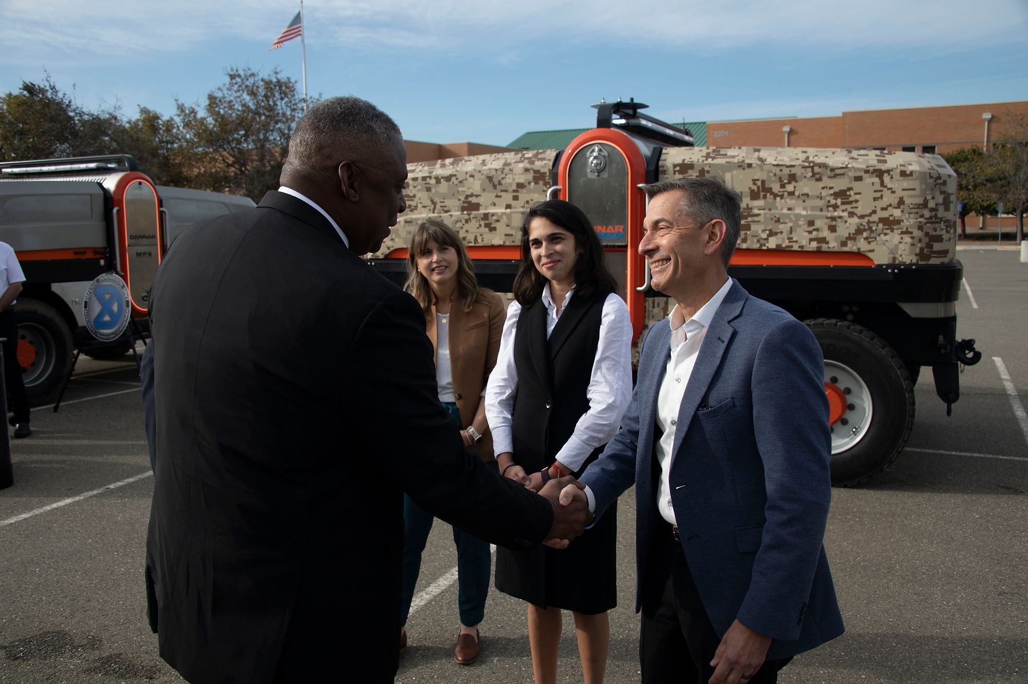 Two men shake hands in front of tactical equipment.