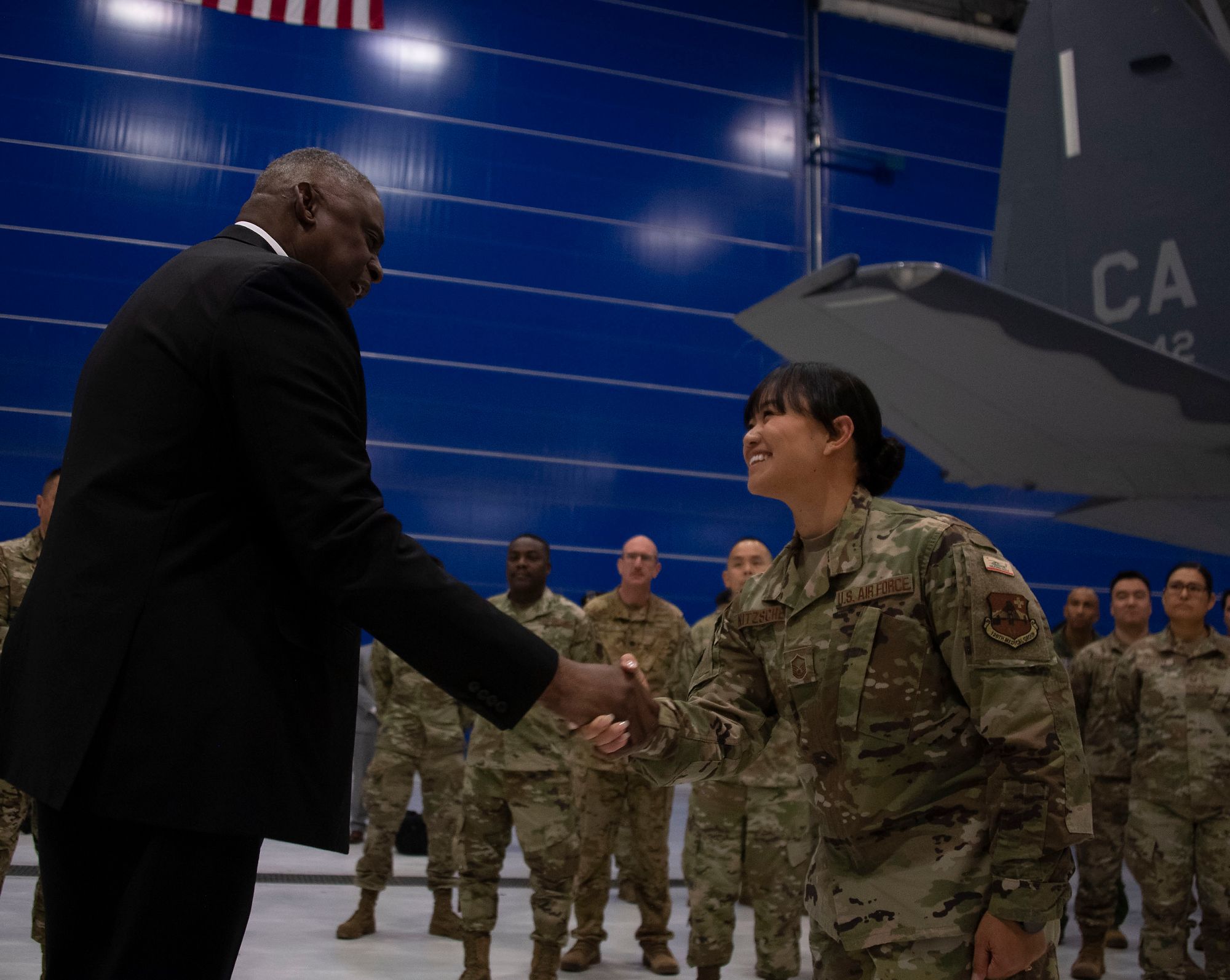 Man in suit presents coin to female Airman.