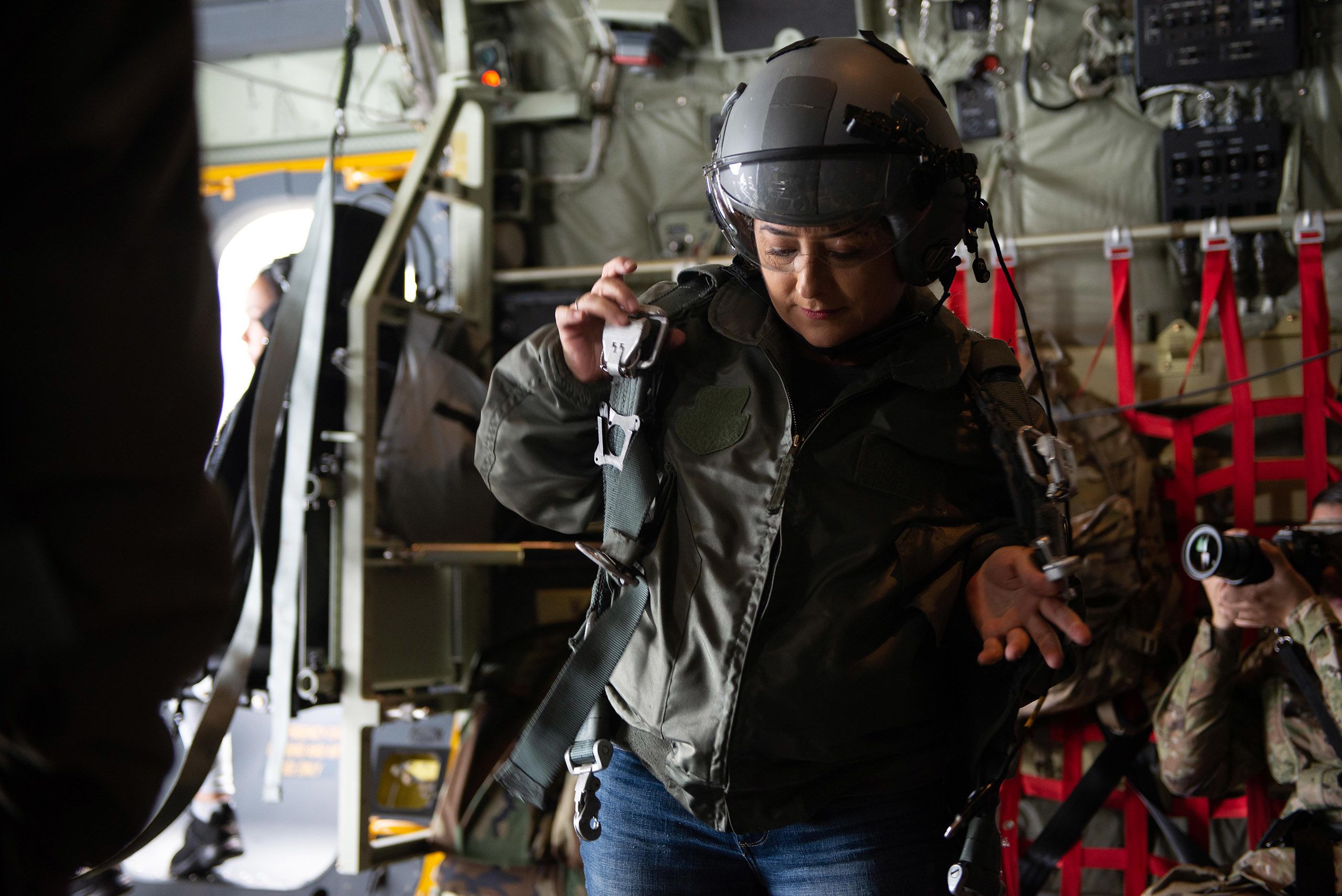Woman wearing helmet puts on military flight harness.