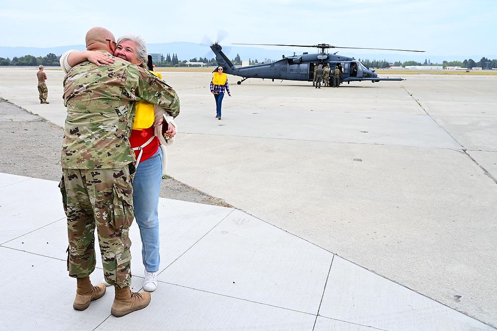 Man and woman hug with helicopter in background.
