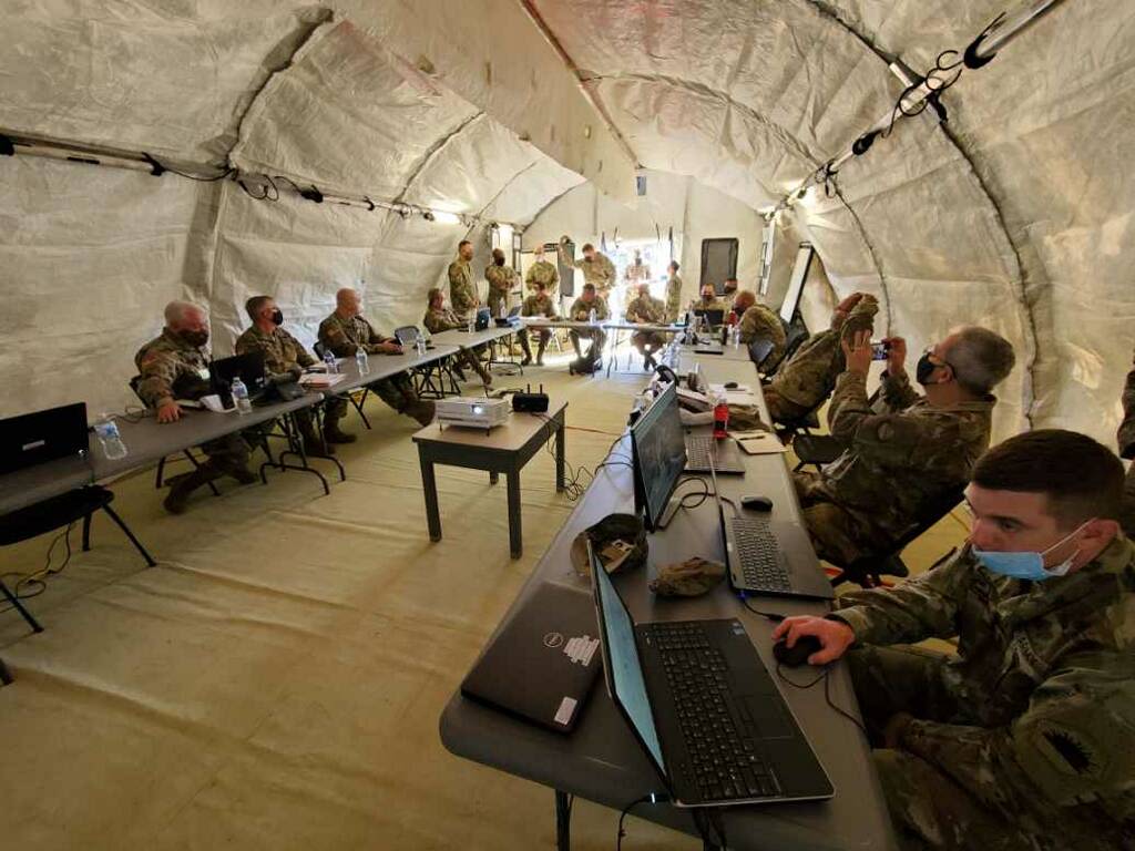 Service members in a large tent working on laptops.
