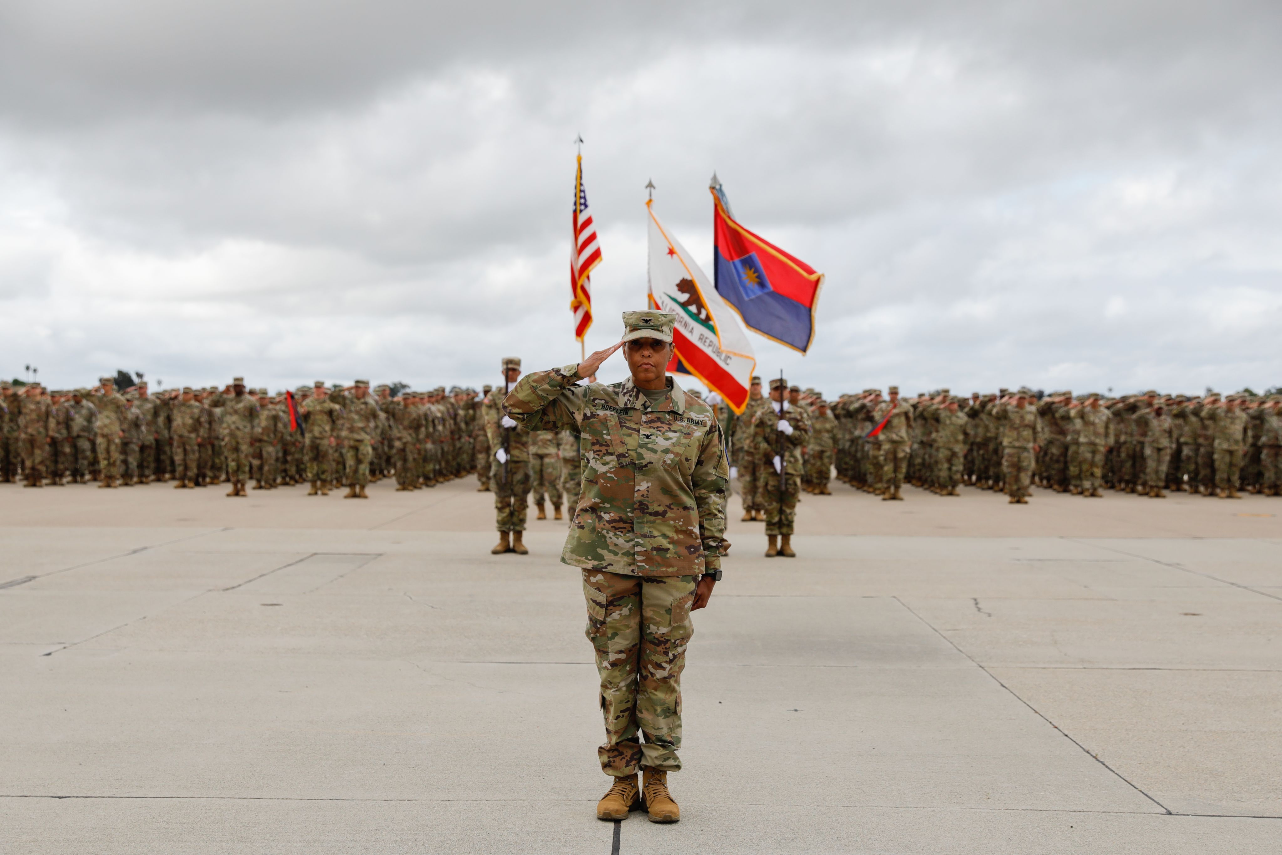 Woman Army officer salutes with formation and color guard behind her