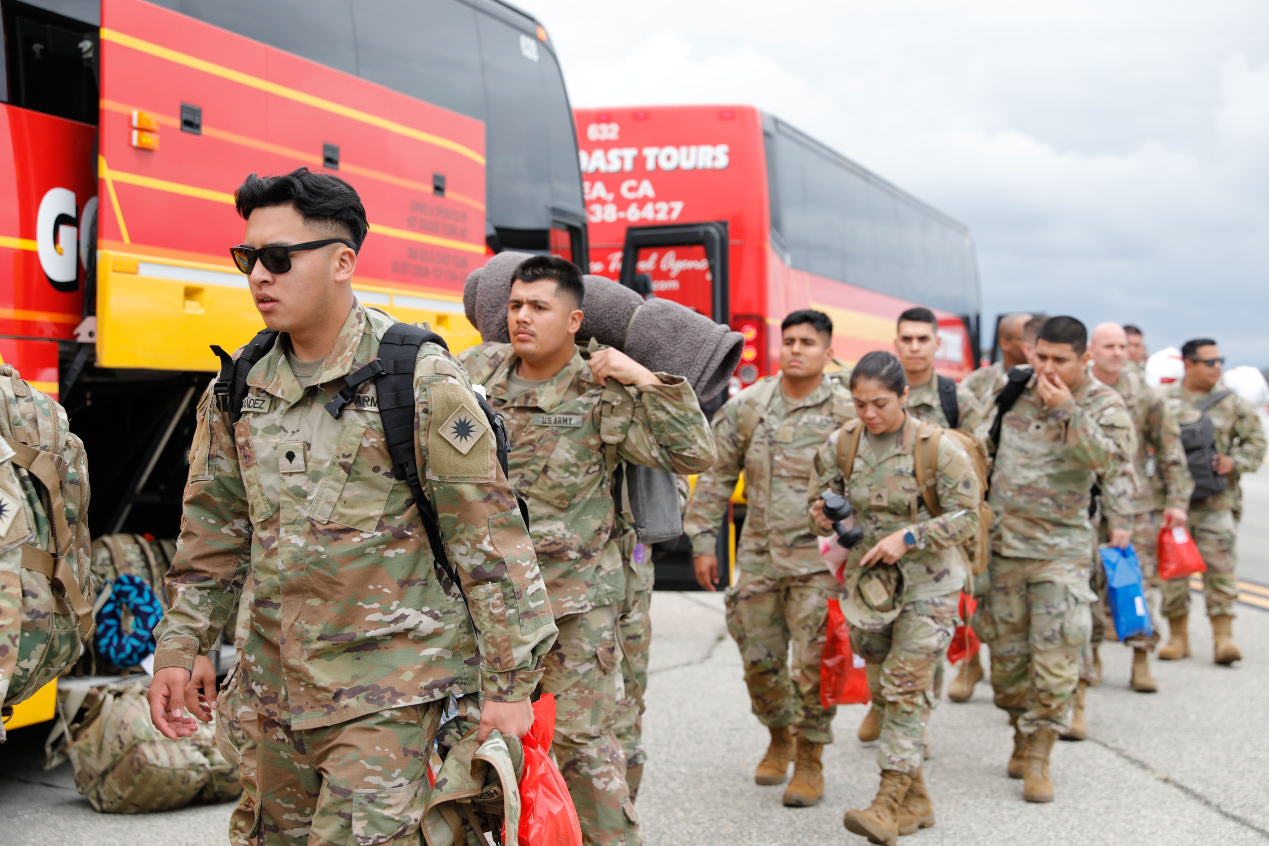 Soldiers with backpacks load onto a commercial bus