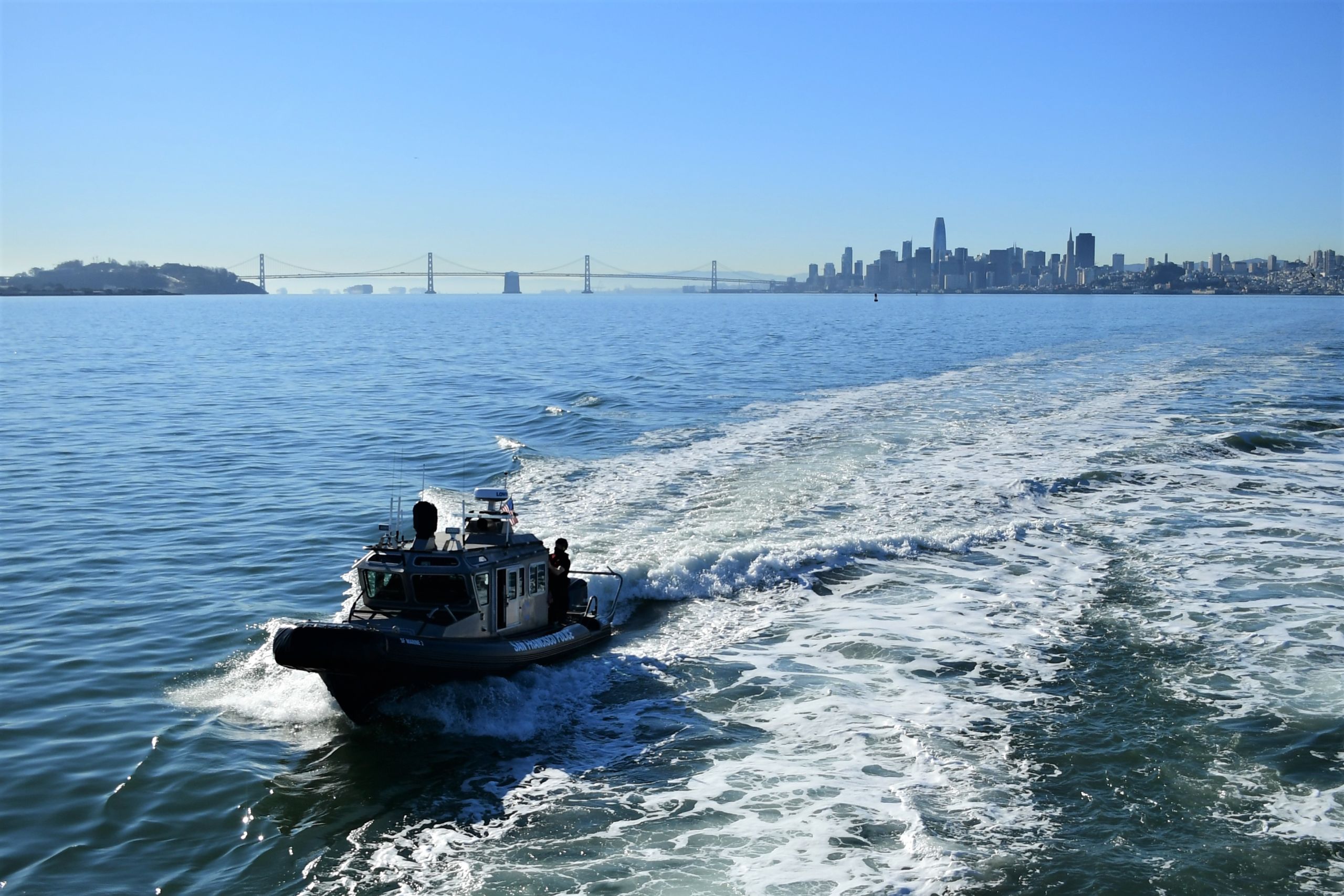A police patrol boat speeds up to a ferry in San Francisco Bay.