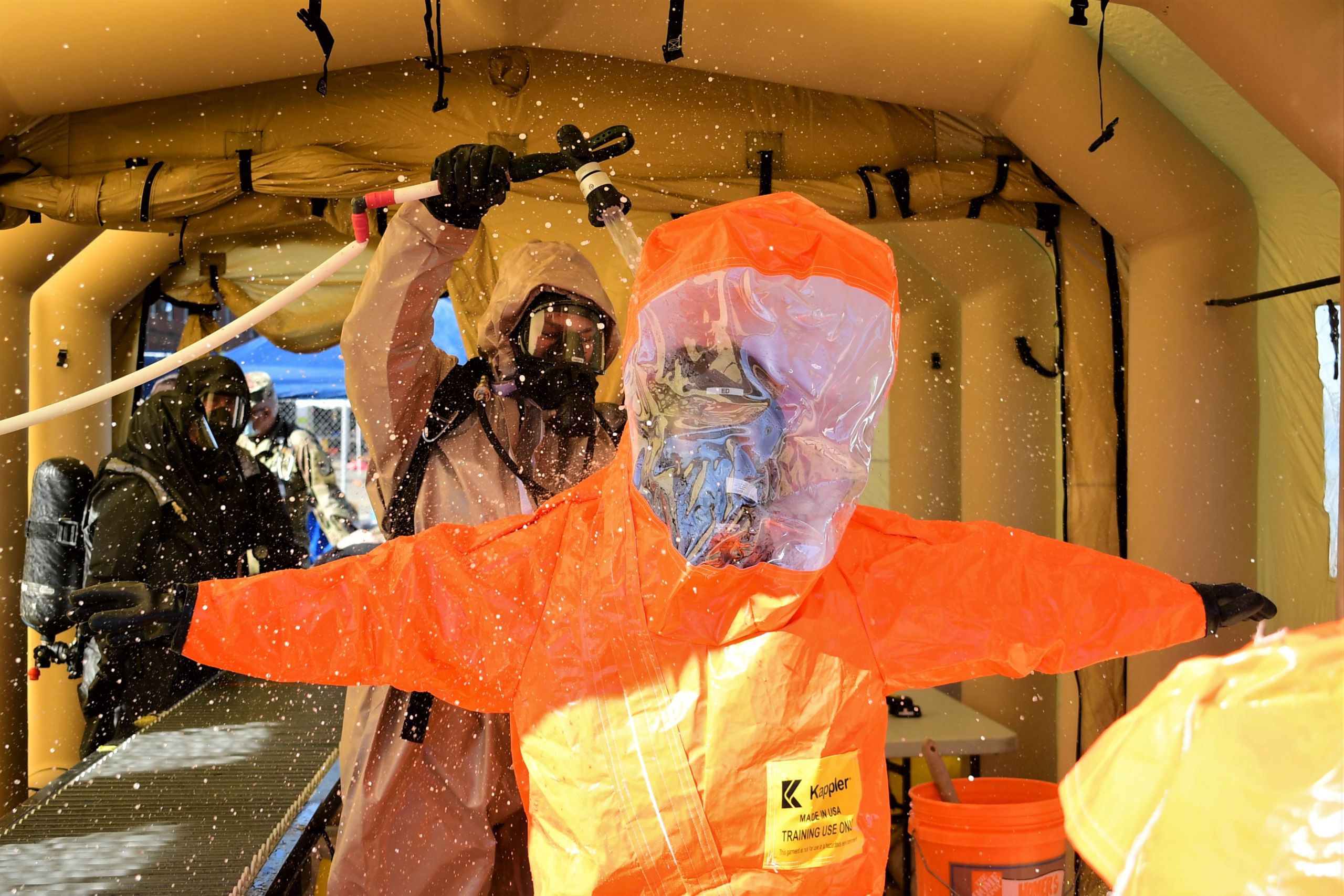 Hazmat suit clad servicemembers wash one another down in order to decontaminate themselves from a hazardous environment.