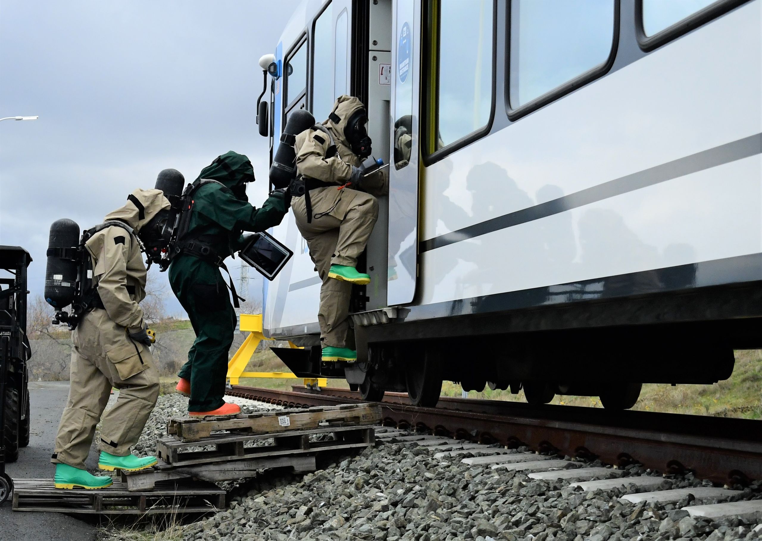 Soldiers in hazardous material suits and oxygen tanks step into a train.