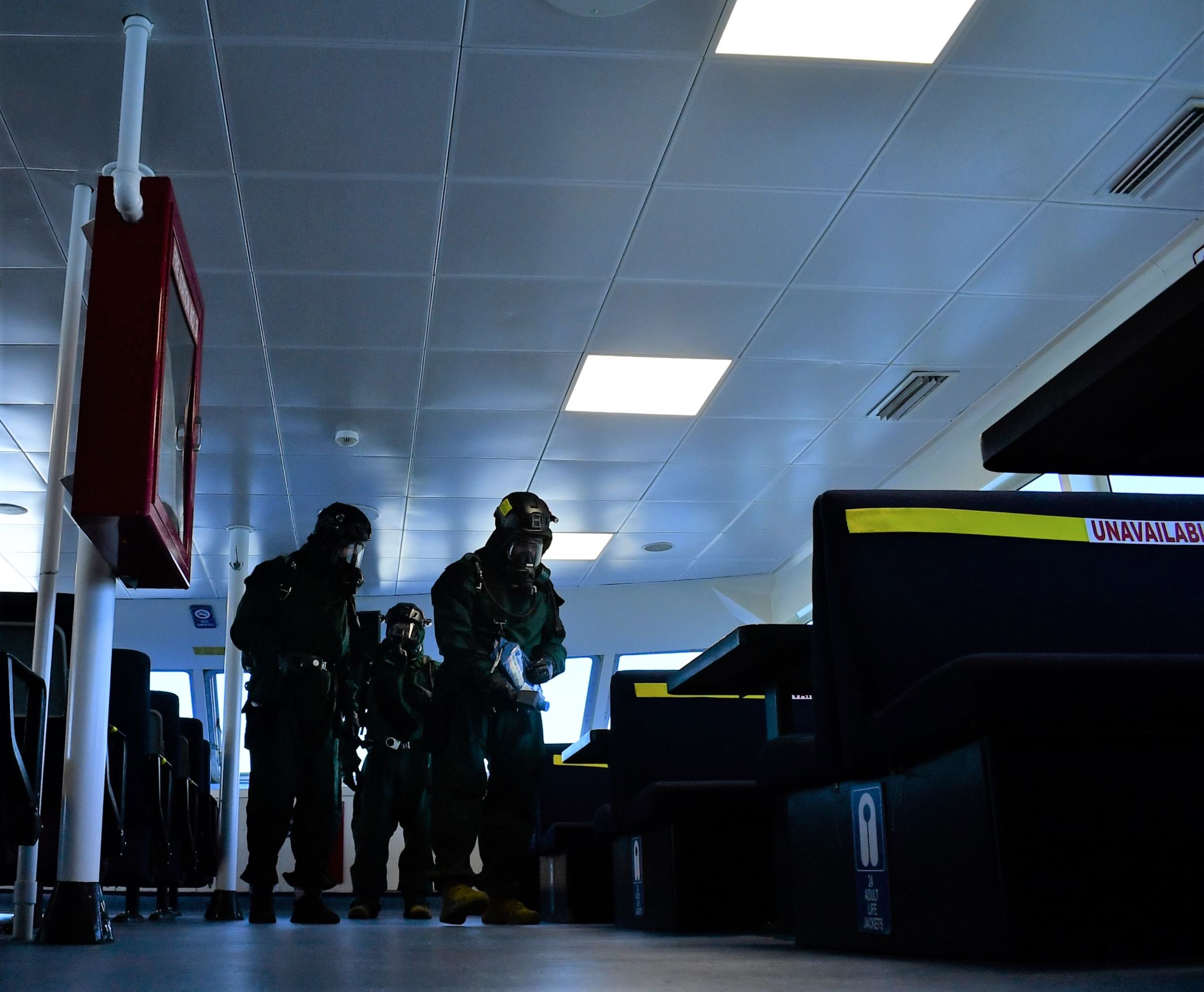 Servicemembers in hazmat suits investigate the passenger compartment of a ferry boat.