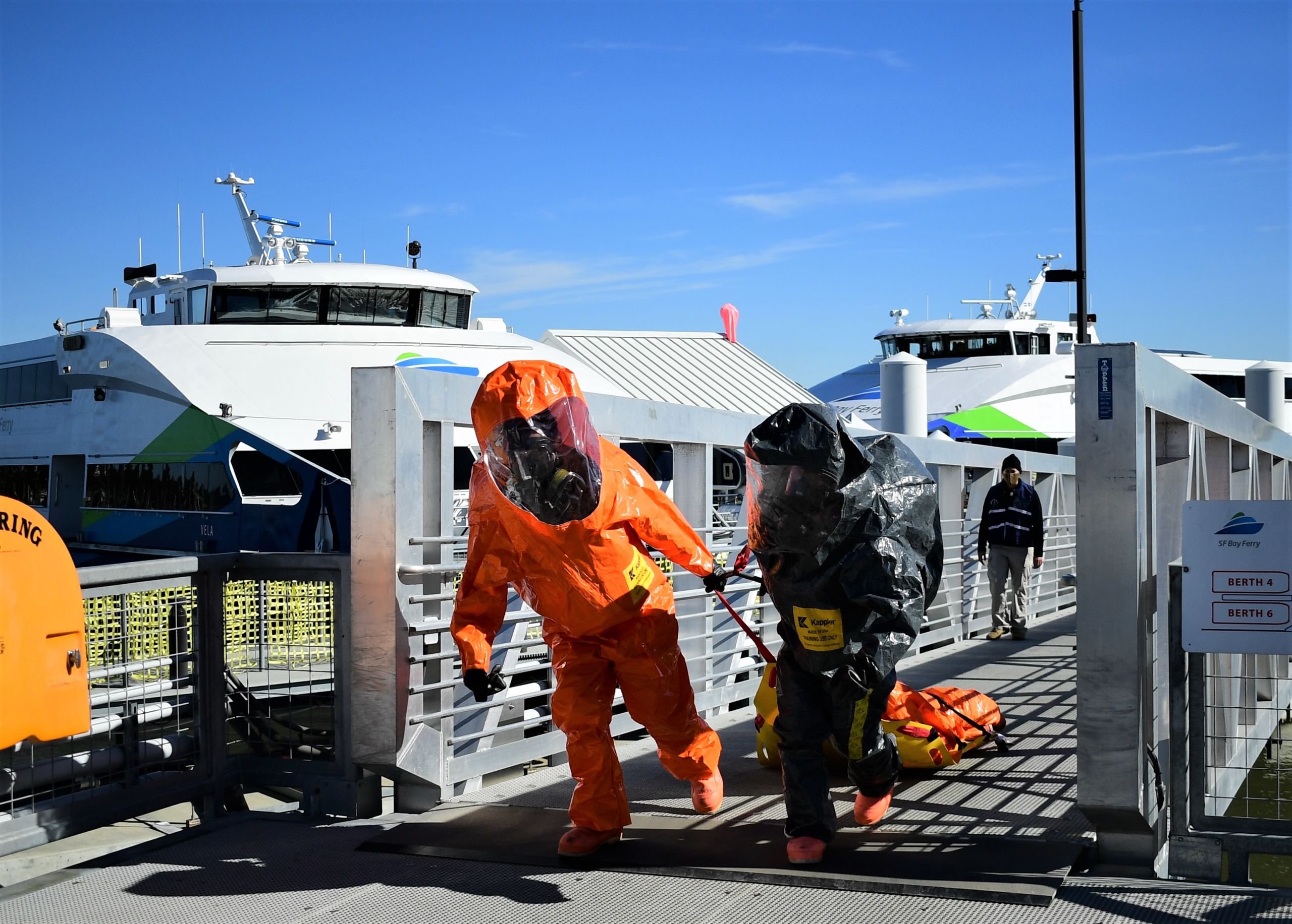 Servicemembers in hazmat suits drag a person behind them to safety from a ferry boat at port.