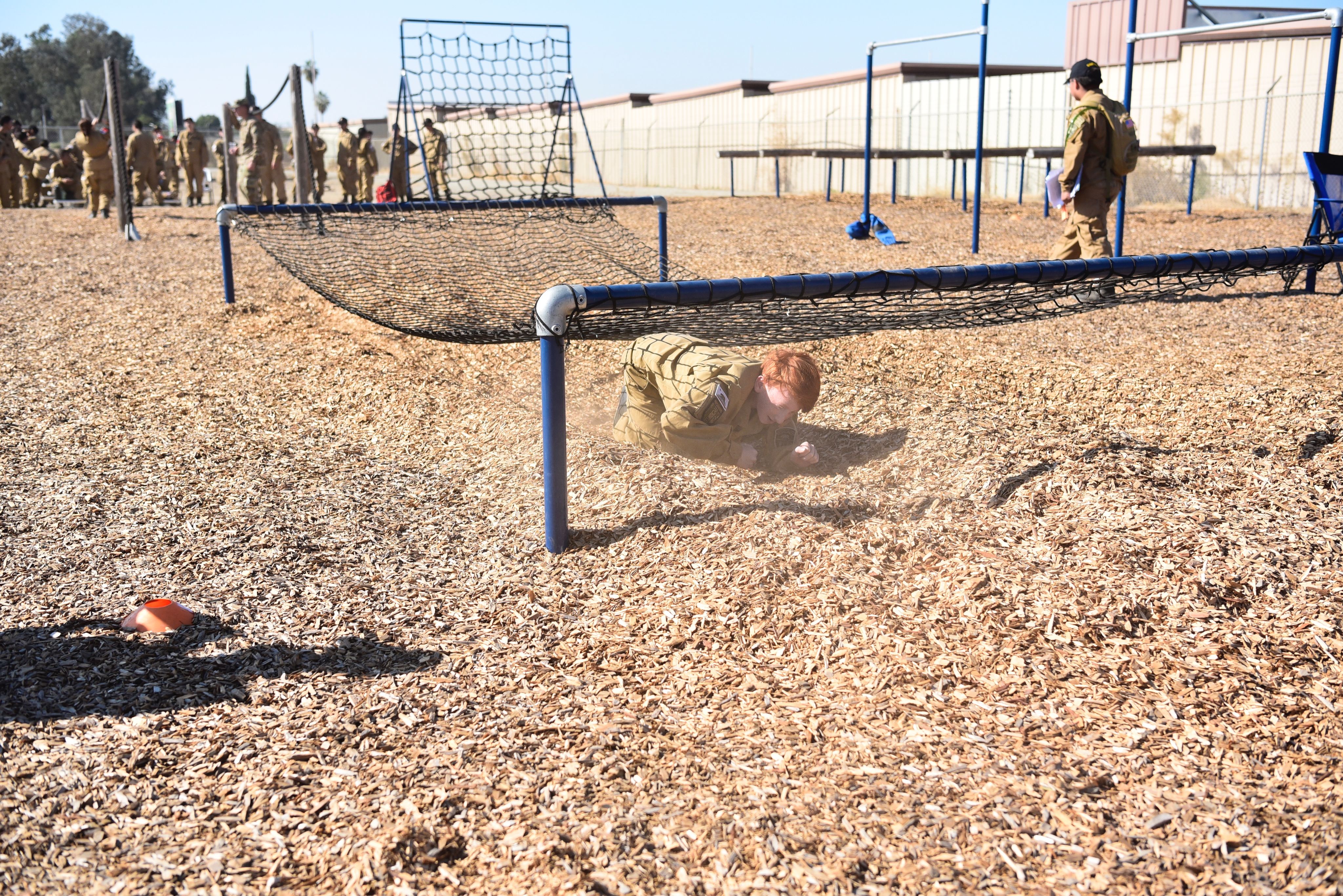 A cadet crawls under a rope wall.