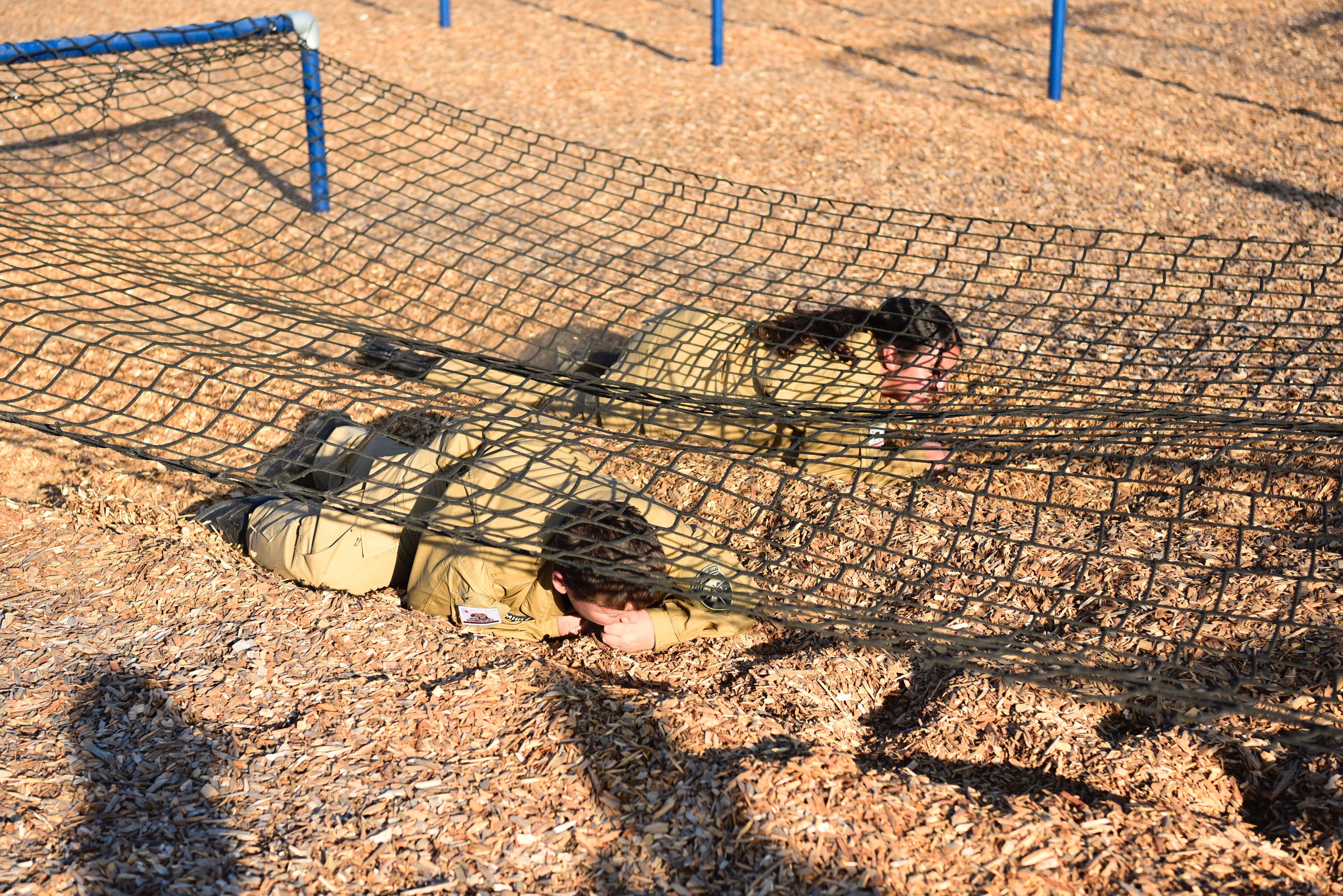 two cadets crawl under rope net.
